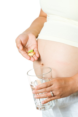 An isolated shot of a pregnant woman taking her drugs/vitamin with a glass of waterの写真素材