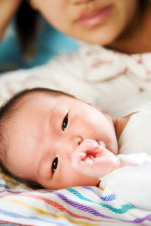 A mother watching her newborn baby sucking his thumbの写真素材