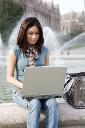 A portrait of a beautiful young woman working on her laptop outdoorの写真素材