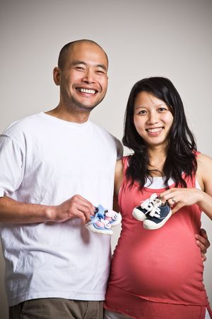 A happy expecting asian couple holding their unborn  shoesの写真素材