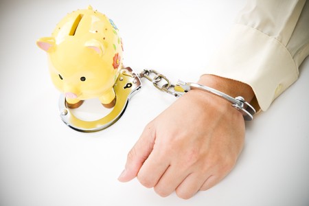 A conceptual shot of a businessman tied up with handcuffs to a piggy bank, can be used to represent financial trouble conceptの写真素材