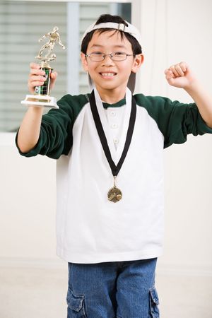 An asian boy excited aboyt his winning sport medal and trophyの写真素材
