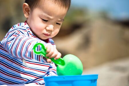 A cute asian boy playing with sand on the beachの写真素材