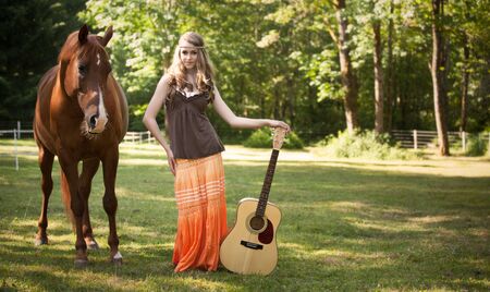 A portrait of a caucasian girl with her guitar and her horseの写真素材