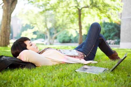 Mixed race college student sleeping on the grass at campusの写真素材