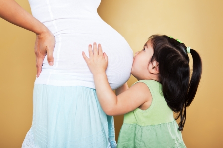 A shot of a little Asian girl kissing her pregnant mother on the stomachの写真素材