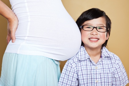 A shot of a little Asian boy listening to the belly of her pregnant motherの写真素材