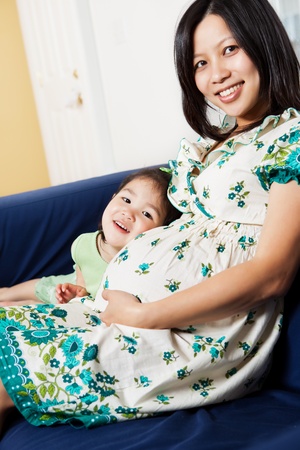 A shot of a pregnant Asian woman sitting on the couch with her daughterの写真素材