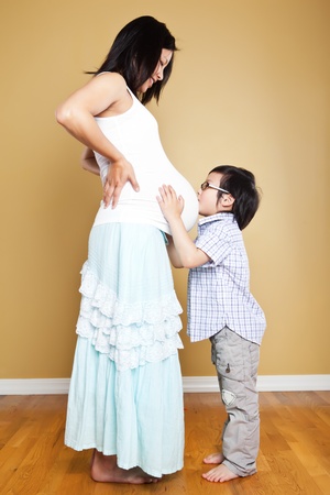 A shot of an Asian boy kissing the belly of his pregnant motherの写真素材