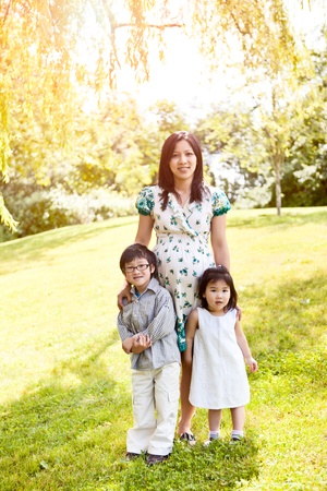 A shot of a pregnant Asian mother with her two kids outdoorの写真素材