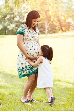 A shot of a little Asian girl kissing her pregnant mother on the bellyの写真素材