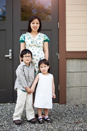 A shot of a pregnant Asian mother with her two kids outdoorの写真素材