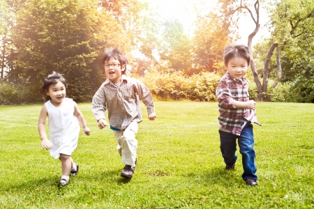 A shot of three Asian kids running in a park (focus in the middle kid)の写真素材