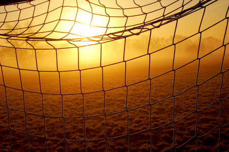 A detail of a net of a soccer goal with the sun and some fog in the background
