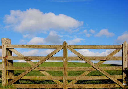 Inlet gutter to a meadow with a wooden fence, green grass and blue sky and cloudsの写真素材