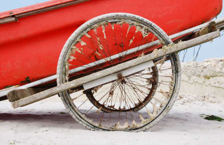 Boat trailer with sandy wheels and red boat on the beachの写真素材