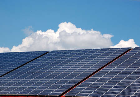 Blue solar energy panels on a roof with sky and sclouds