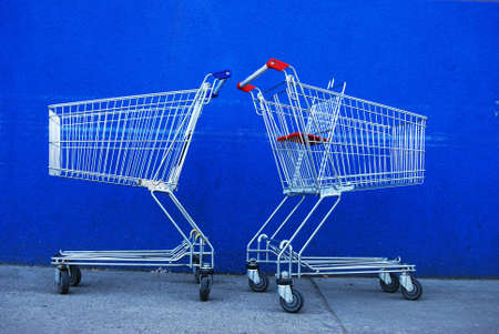 Two silver shopping baskets in front of a blue wallの写真素材