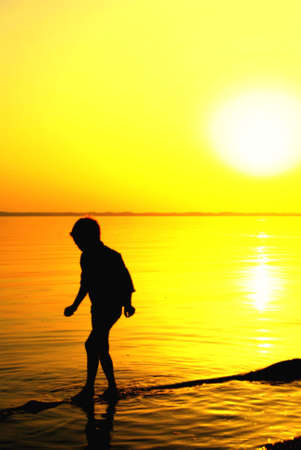 Young boy playing in the water during sundownの写真素材