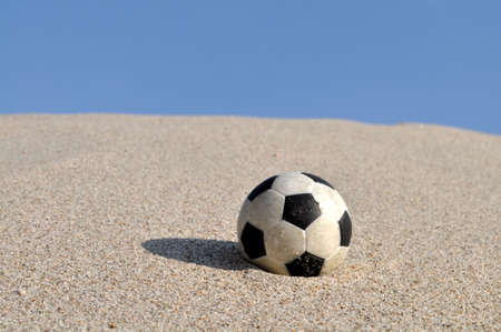 Football in the sand with a blue skyの写真素材