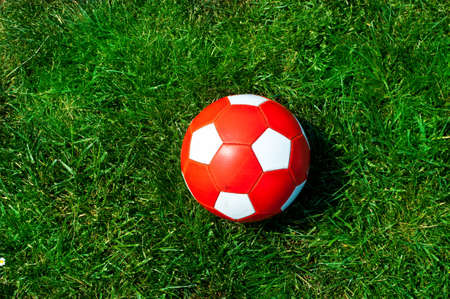 Red soccer ball with white dots on green grassの写真素材