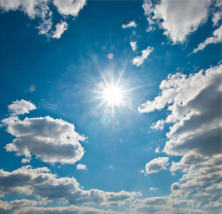 Bright sun with rays in a blue sky with cloudsの写真素材