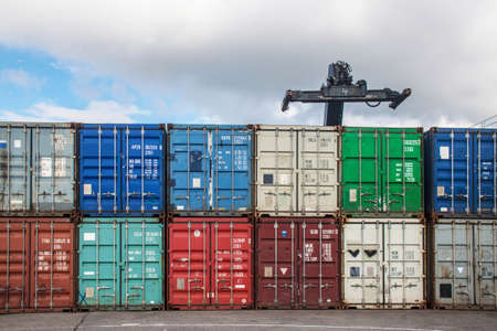 Lifting arm of a crane aboe a colorful row of cargo containerのeditorial素材