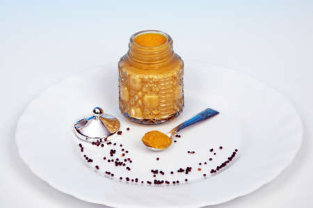 English mustard in a glass mustard pot with mustard seeds in the foreground 