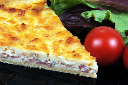 Quiche Lorraine with lettuce and cherry tomatoes on a black plate の写真素材