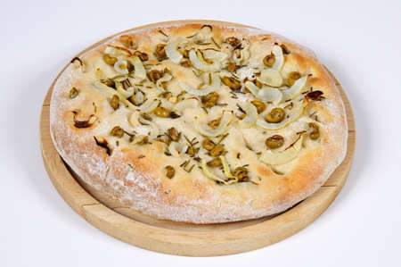 Italian Focaccia bread on a wooden chopping board topped with green olive, onion and rosemary against a white background の写真素材