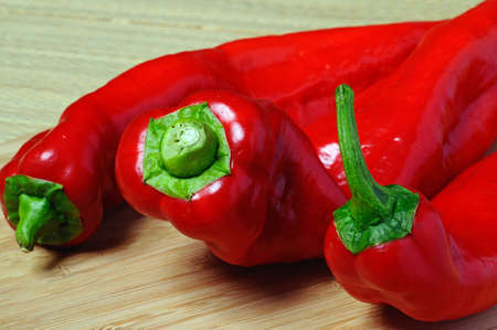 Three red Italian pointed peppers on a wooden chopping board の写真素材