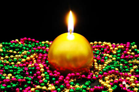 Round gold Christmas candle sitting in colourful beads set against a black background の写真素材