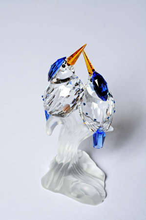 Two glass crystal kingfishers sitting on a branch against a plain background の写真素材
