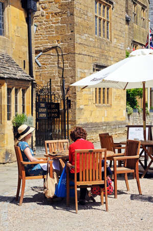 Broadway, UK - June 12, 2014 - Two women sitting at a pavement cafe by the Lygon Arms Hotel along...