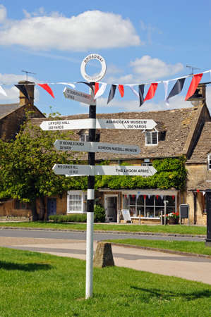Broadway, United Kingdom - June 12, 2014 - Black and white signpost on the village green along the High Street giving directions to tourist attractions, Broadway, Cotswolds, Worcestershire, England, UK, Western Europe のeditorial素材