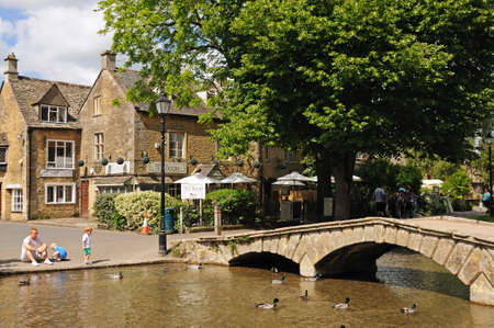 Stone footbridge across the River Windrush with tea-rooms to the rear, Bourton on the Water,...