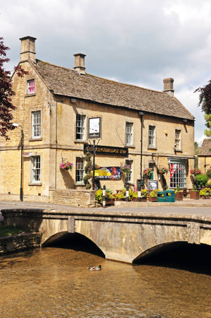 Bourton-on-the-Water, UK - June 12, 2014 - Stone footbridge across the River Windrush with the Kingsbridge Inn to the rear, Bourton on the Water, Gloucestershire, England, UK, Western Europe.のeditorial素材