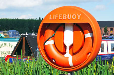 Barton-under-Needwood, UK - May 21, 2014 - Lifebuoy with narrowboats to the rear moored in the canal...