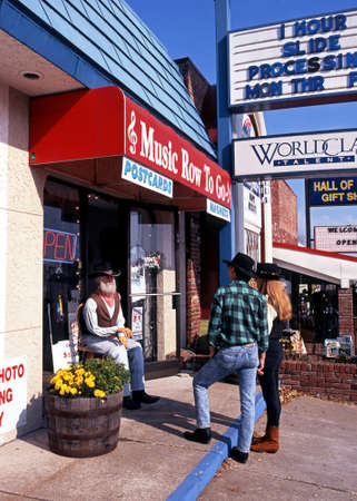 Cowboy couple looking at a statue of an old man cowboy sitting on a chair outside a shop along Music Row, Nashville, Tennessee, USA.のeditorial素材