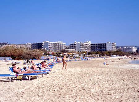 Tourists relaxing on the sandy beach with hotels to the rear Ayia Napa Cyprus.のeditorial素材