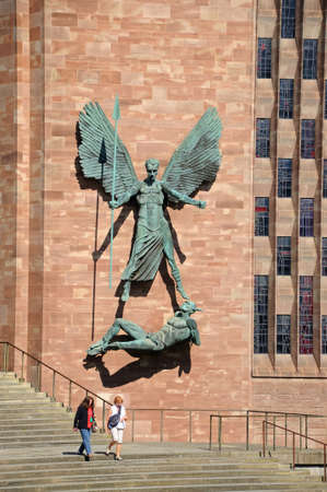 Statue of St Michael holding a spear over the devil Michael and the Devil on the wall of the new Cathedral, Coventry, West Midlands, England, UK, Western Europe.のeditorial素材