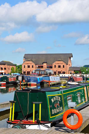 Narrowboats on their moorings in the canal basin with shops, bars and restaurants to the rear, Barton Marina, Barton-under-Needwood, Staffordshire, England, UK, Western Europe.のeditorial素材
