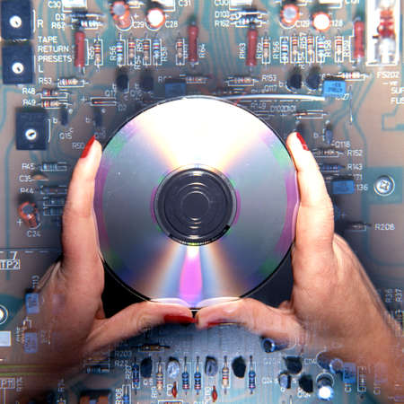Hands holding a CD above an electonic circuit, UK, Western Europe.のeditorial素材