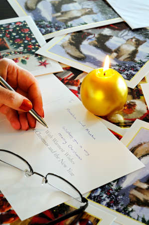 Writing Christmas cards by candlelight with cards scattered on the table.のeditorial素材