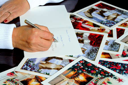 Woman writing Christmas cards with cards scattered around the tableのeditorial素材
