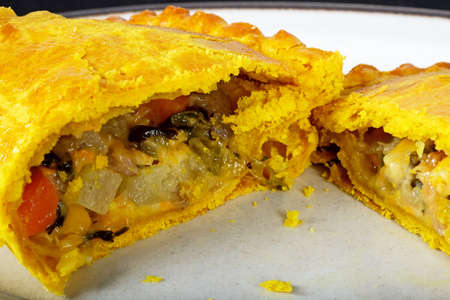 Vegetarian pasty cut in half filled with cheddar cheese, onion, carrot, swede, potato and sweet potato in an all butter pastry flavoured with turmeric.の写真素材