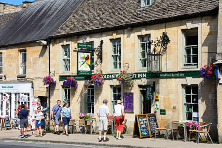 View of The Golden Pheasant Inn along The Hill shopping street with tourists passing by, Burford,...