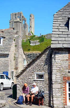Couple sitting on a bench in village centre with the castle to the rear, Corfe, Dorset, England, UK, Western Europe.のeditorial素材