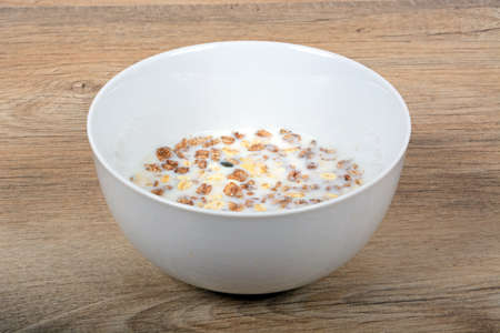 Muesli with a mix of healthy fruit, nuts and seeds and milk in a dish against a wooden background.の写真素材