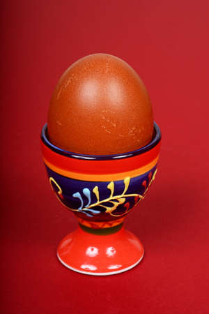 A boiled egg in a decorative ceramic eggcup against a red background.